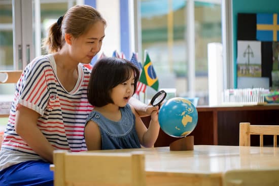 Asian girl looking at globe while listening to teacher