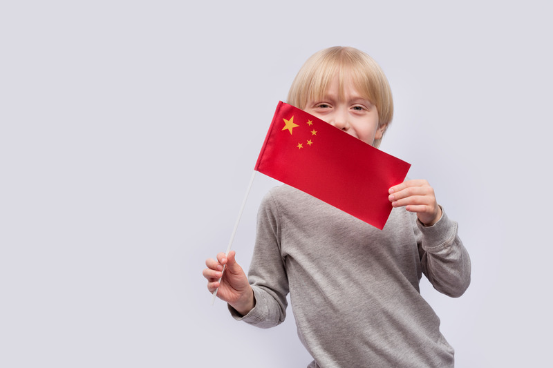 Portrait of child on white background with flag of China in hands. Learning Chinese language for kids