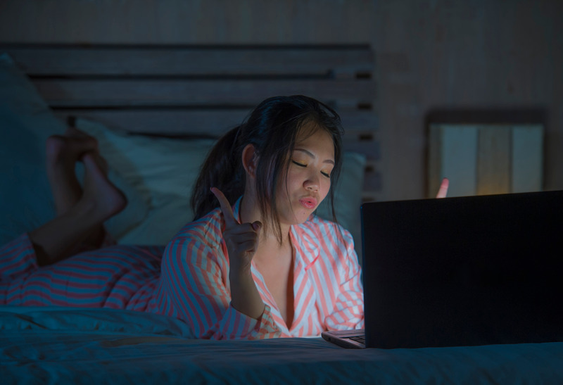 lifestyle portrait of young beautiful and happy Asian Chinese student girl watching online movie or enjoying social media with laptop computer on bed late at night in internet addiction concept